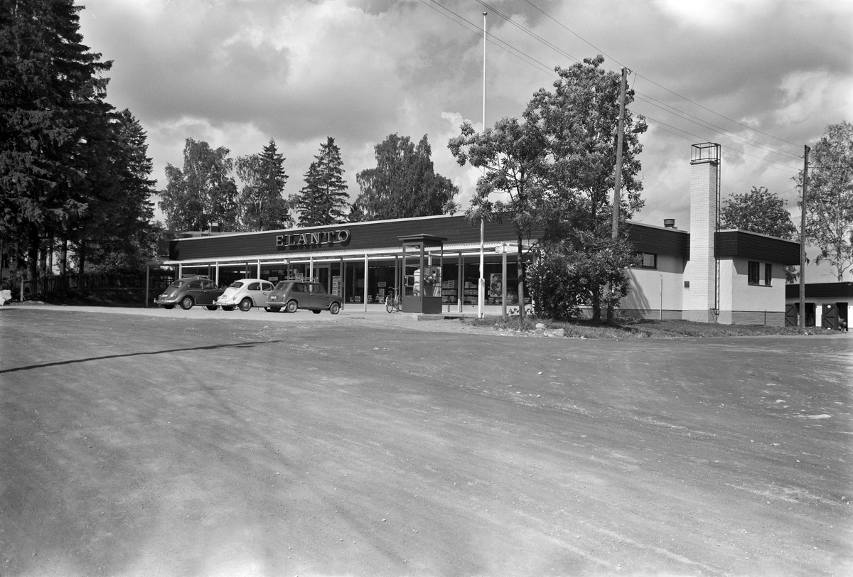 sisällön kuvaus: Puistolantie 26. Laaksotie. (= Puistolantori 4) Suurmetsä Puistola. Elannon myymälä, jonka edessä puhelinkoppi. mustavalkoinen